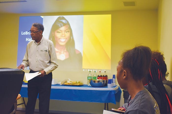 Resident Services Director speaking in front of a projector showing the face of a recent female graduate